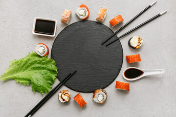 Frame made of board with tasty sushi rolls, chopsticks and soy sauce on grey background