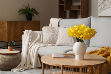 Interior of stylish living room with grey sofa, plaid, coffee table and flowers