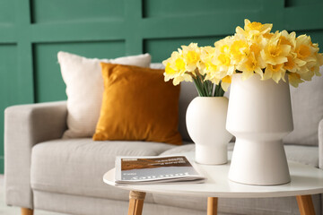 Vases with daffodils and magazine on table in living room, closeup