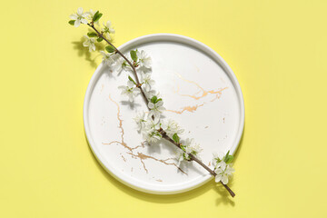 Beautiful plate with blossoming branch on yellow background