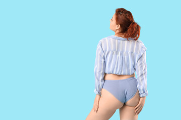 Young woman in period panties on blue background, back view