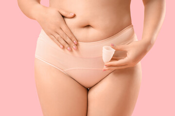 Young woman in period panties holding menstrual cup on pink background