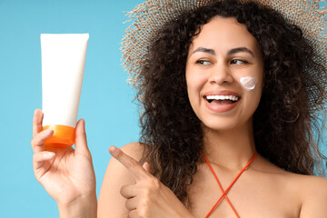 Young African-American woman with sunscreen cream on blue background, closeup