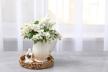 Vase with blossoming branches on table near window in room