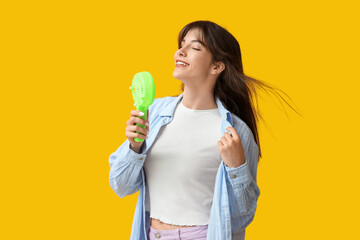 Young woman with mini fan on yellow background