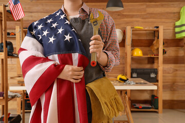 Female carpenter with USA flag and wrench in workshop. Labor Day celebration