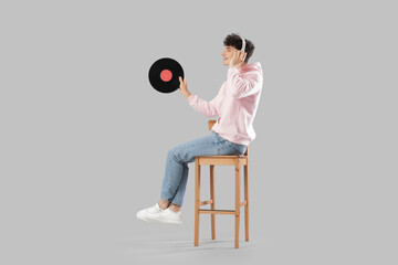 Handsome young man in headphones with vinyl disk listening to music on light background