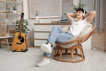 Handsome young man in headphones listening to music on armchair at home