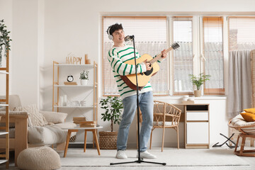 Handsome young man in headphones with guitar singing at home