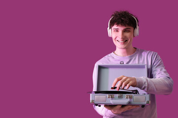 Handsome young man in headphones with record player listening to music on purple background
