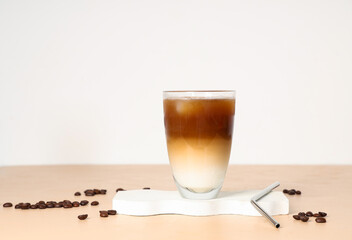 Glass of iced latte and coffee beans on beige table