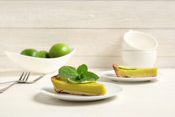 Plates with pieces of tasty lime tart on white wooden background