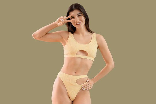 Young woman in swimsuit showing victory gesture on green background