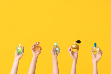 Female hands with many bottles of perfume on yellow background