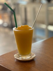 A Glass of Mango Smoothie With a Straw and Stirrer on a Wooden Table