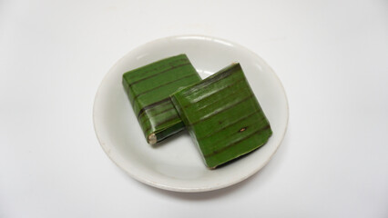 Lemper, a traditional snack from Indonesia, made from sticky rice, steamed with coconut milk, chicken floss inside, and wrapped with banana leaf. Served on white plate, isolated on white background
