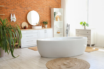Interior of stylish bathroom with bathtub, shelving unit, mirror and sink