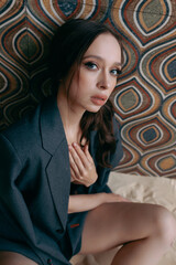 Fototapeta premium Young sexy woman in an unbuttoned jacket and bare breasts and jeans posing against the wall. Model shooting in an interior studio with sand on the floor.