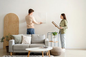 Young couple hanging paintings on light wall at home