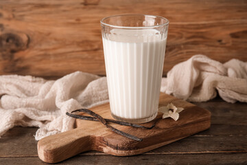 Glass of fresh vanilla milk with sticks and flower on wooden background
