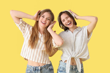 Female friends in headphones listening to music on yellow background