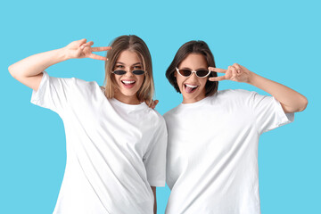 Female friends in sunglasses showing victory gesture on blue background