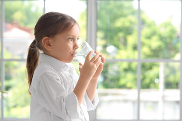 Cute little girl drinking water near window at home