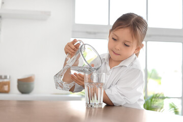 Cute little girl pouring water into glass in kitchen