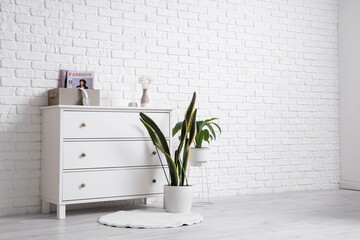 Chest of drawers with houseplants and decor near white brick wall