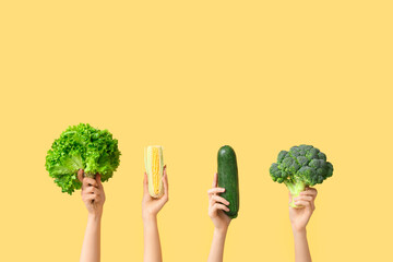 Female hands holding fresh vegetables on yellow background