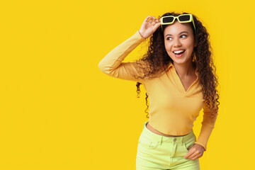 Beautiful African-American woman with sunglasses on yellow background