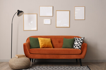 Interior of living room with brown sofa, standard lamp and blank frames hanging on grey wall