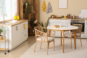 Interior of modern kitchen with dining table, white counters and blank frames hanging on beige wall