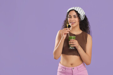 Beautiful young happy African-American woman with glass of tasty kiwi smoothie on purple background