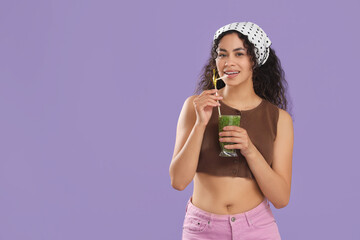 Fototapeta premium Beautiful young happy African-American woman with glass of tasty kiwi smoothie on purple background
