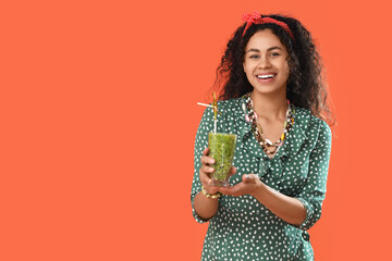 Beautiful young happy African-American woman with glass of tasty kiwi smoothie on orange background