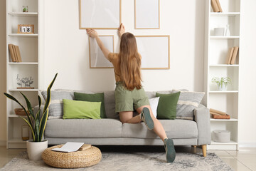 Young woman hanging frame on wall in living room