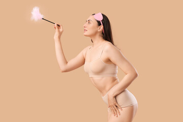 Beautiful young woman in underwear with feather stick and mask from sex shop on beige background