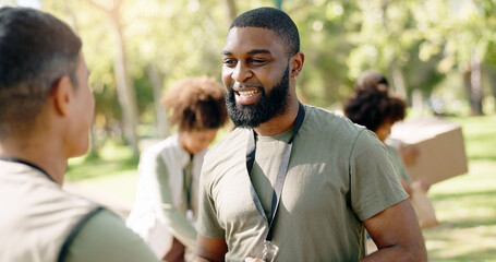 Happy man, volunteer and talking with colleague in nature for charity or community service at outdoor park. Male person with smile or team in NGO for mission, food or supplies on earth day in forest
