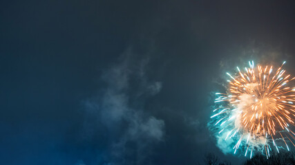 Bright fireworks illuminate night sky, casting a glow of blue and yellow hues. The image conveys...