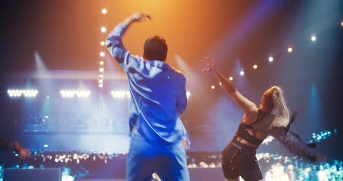 Creative Pop Artist Performing a Hit Song on Stage with Two Striking Female Dancers, Inspiring a Large Audience in a Colorful Neon Concert Setting with Cinematic Lighting and Enthusiastic Crowd