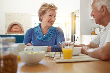 Senior, couple and happy with eating at breakfast in dining room for nutrition, healthy meal and retirement. Elderly, people and smile in home with conversation, relax or morning routine in apartment