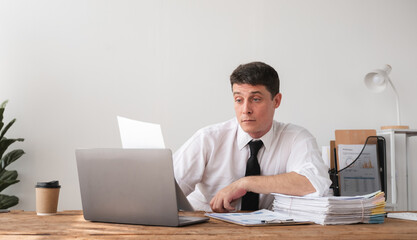 Businessman reviewing documents at desk with laptop and financial reports, concept of focus and workload