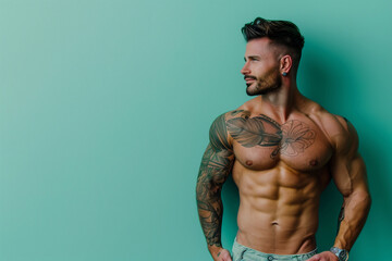 Fototapeta premium A muscular man stands in front of a blue wall. He is posing for a picture, and his chest is showing