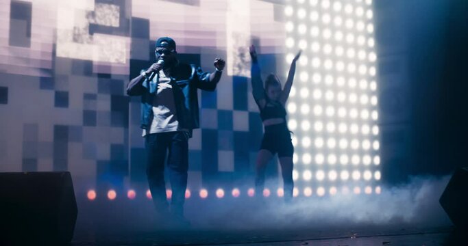 Creative Rap Artist Performing a Hit Song on Stage with a Striking Female Dancer, Inspiring a Large Audience in a Colorful Neon Concert Setting with Cinematic Lighting and Animated LED Screen