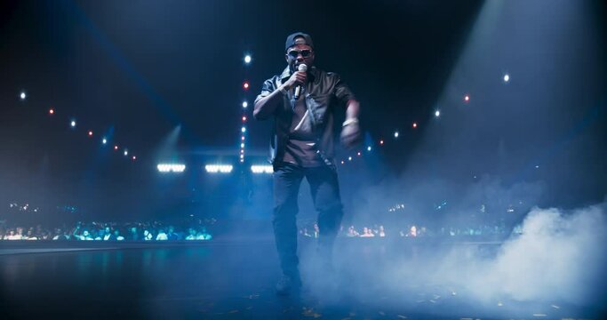 Black Rap Artist Performing Energetic Hip Hop Rhythms on a Talent Show Stage in Front of an Excited Crowd of Fans. Vibrant Visuals and Spectacular Show Make the Concert a Sensory Delight