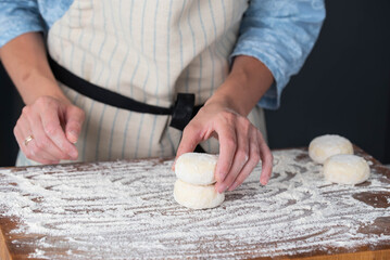 Hands of a female chef preparing homemade syrniki (cottage cheese pancakes)  by coating them in...