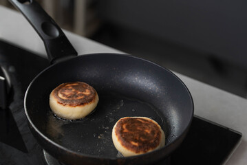 Hands of a female chef frying and baking homemade syrniki in a pan, sizzling in oil. Concept of home cooking, traditional recipes, and culinary preparation.