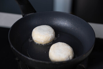 Hands of a female chef frying and baking homemade syrniki in a pan, sizzling in oil. Concept of home cooking, traditional recipes, and culinary preparation.