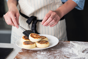 Hands of a female chef placing freshly cooked syrniki on a plate, garnishing with sour cream and mint. Concept of home cooking, traditional recipes, and culinary presentation.